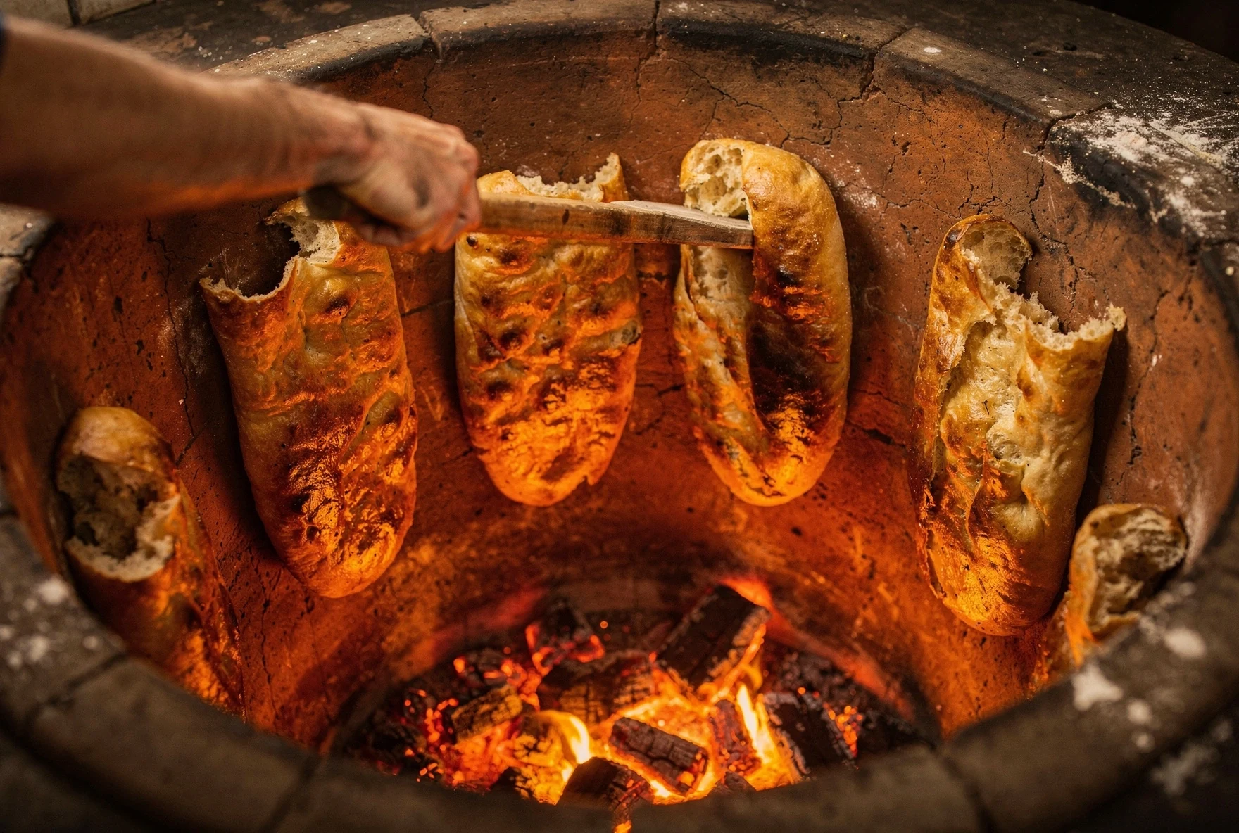 Looking down into a traditional Georgian tone oven with golden shotis puri bread stuck to the clay walls and glowing coals at the bottom