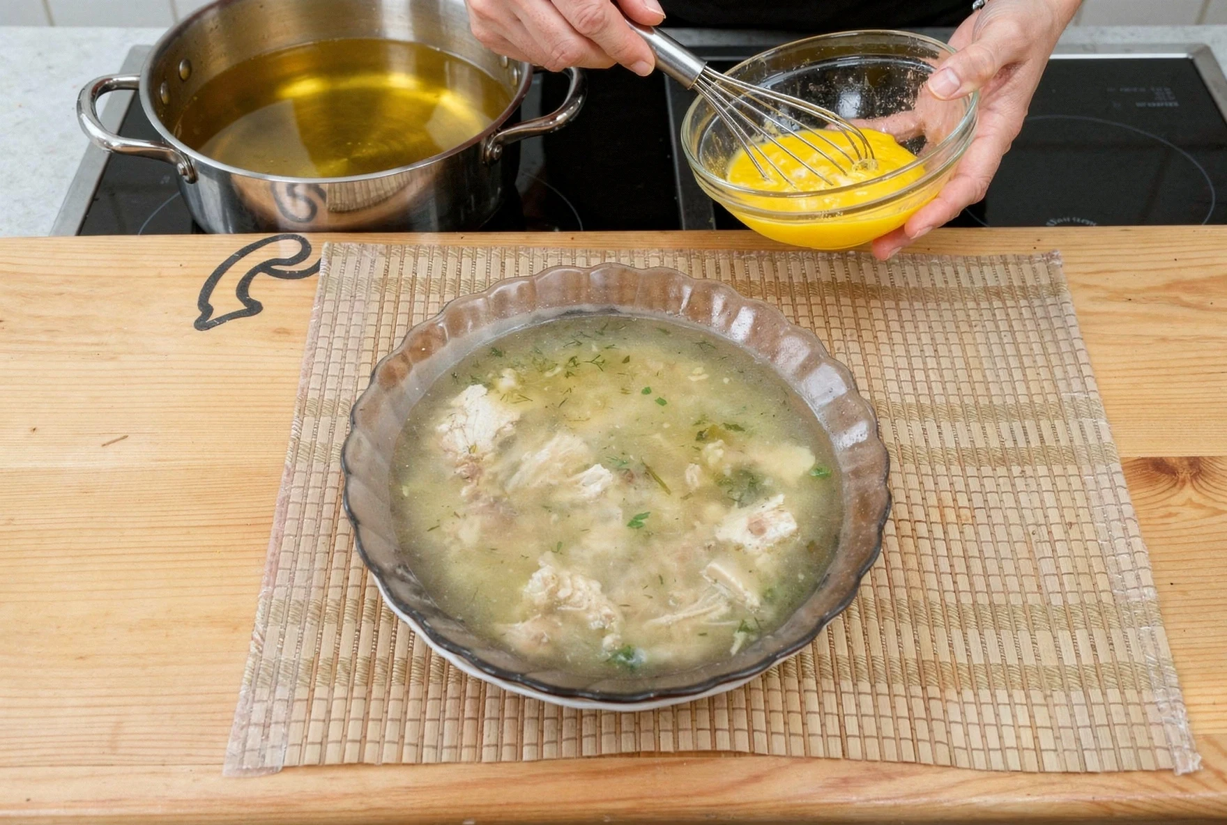 Close-up of egg yolks being tempered with hot broth while whisking