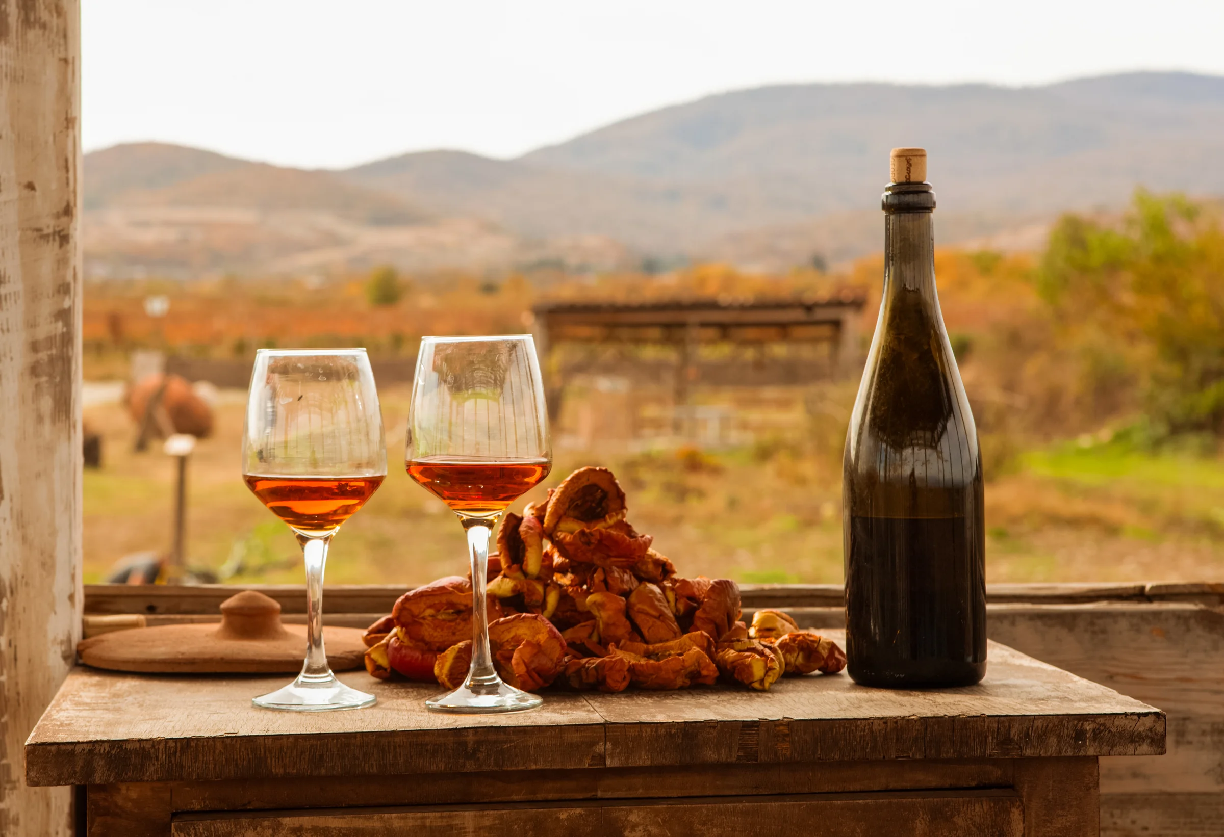 Amber wine glasses and bottle on rustic table overlooking Georgian countryside