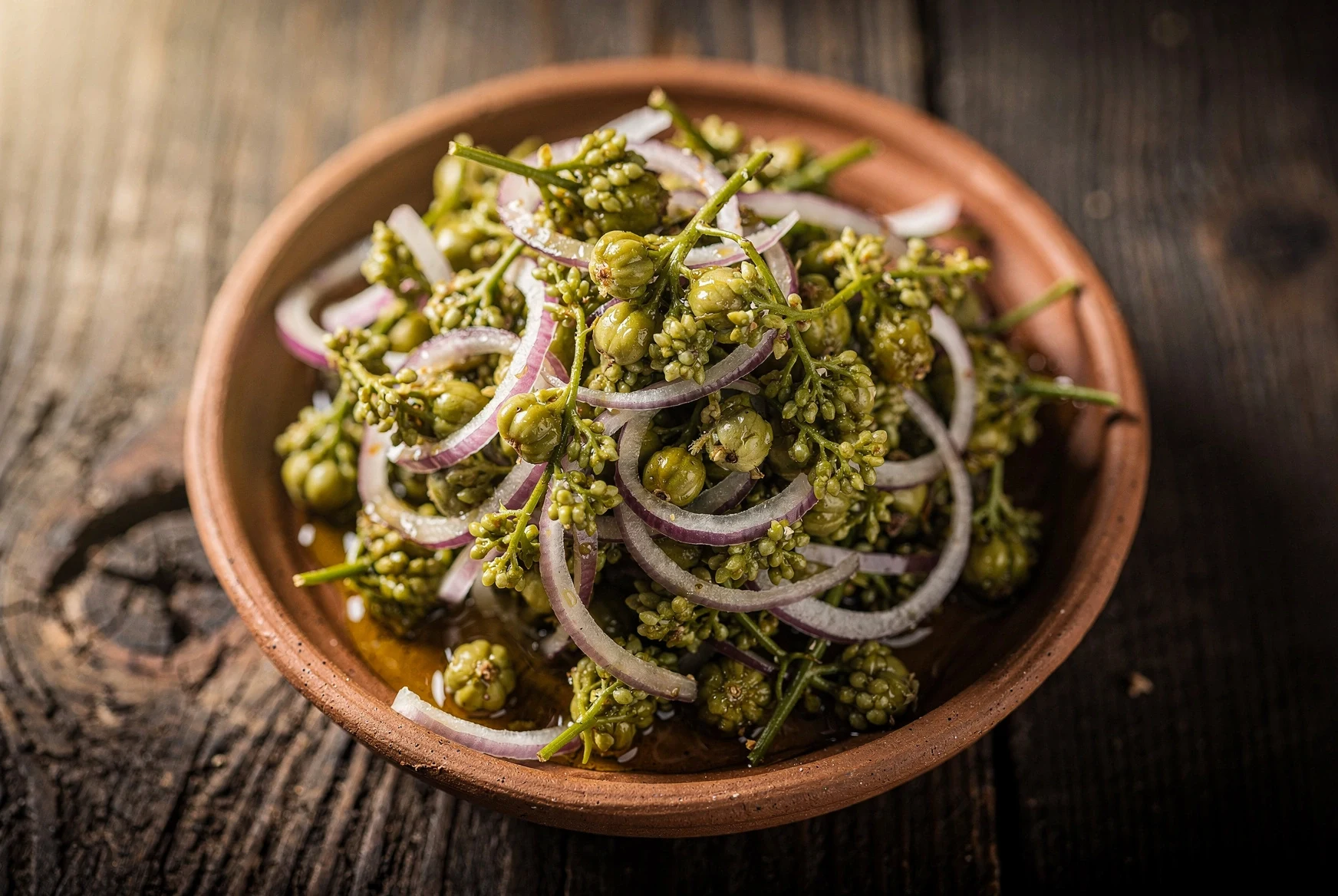 Close-up of dressed jonjoli in a clay bowl with thin red onion