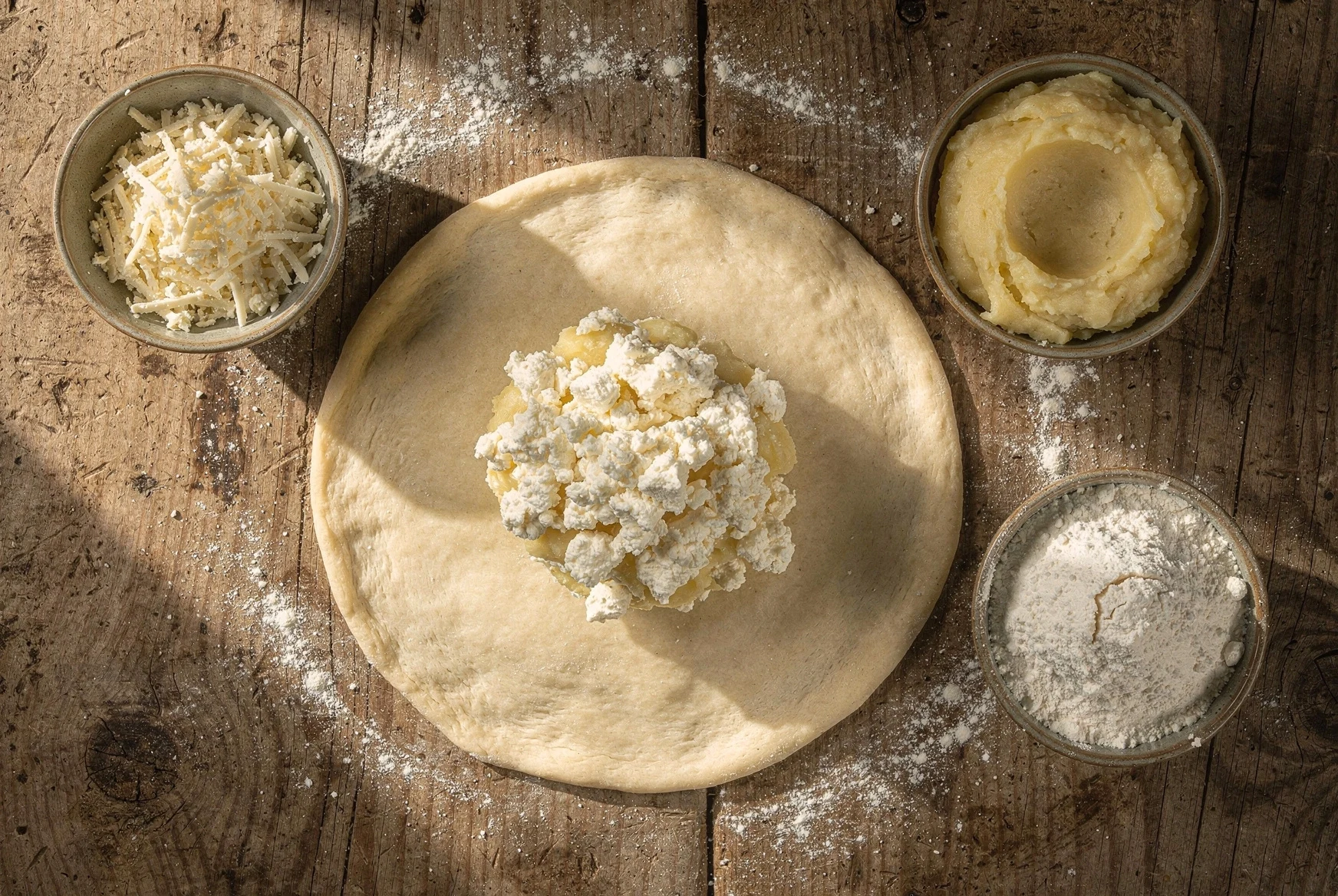 Overhead preparation of khabidzgina with round dough and potato-cheese filling on a wooden table