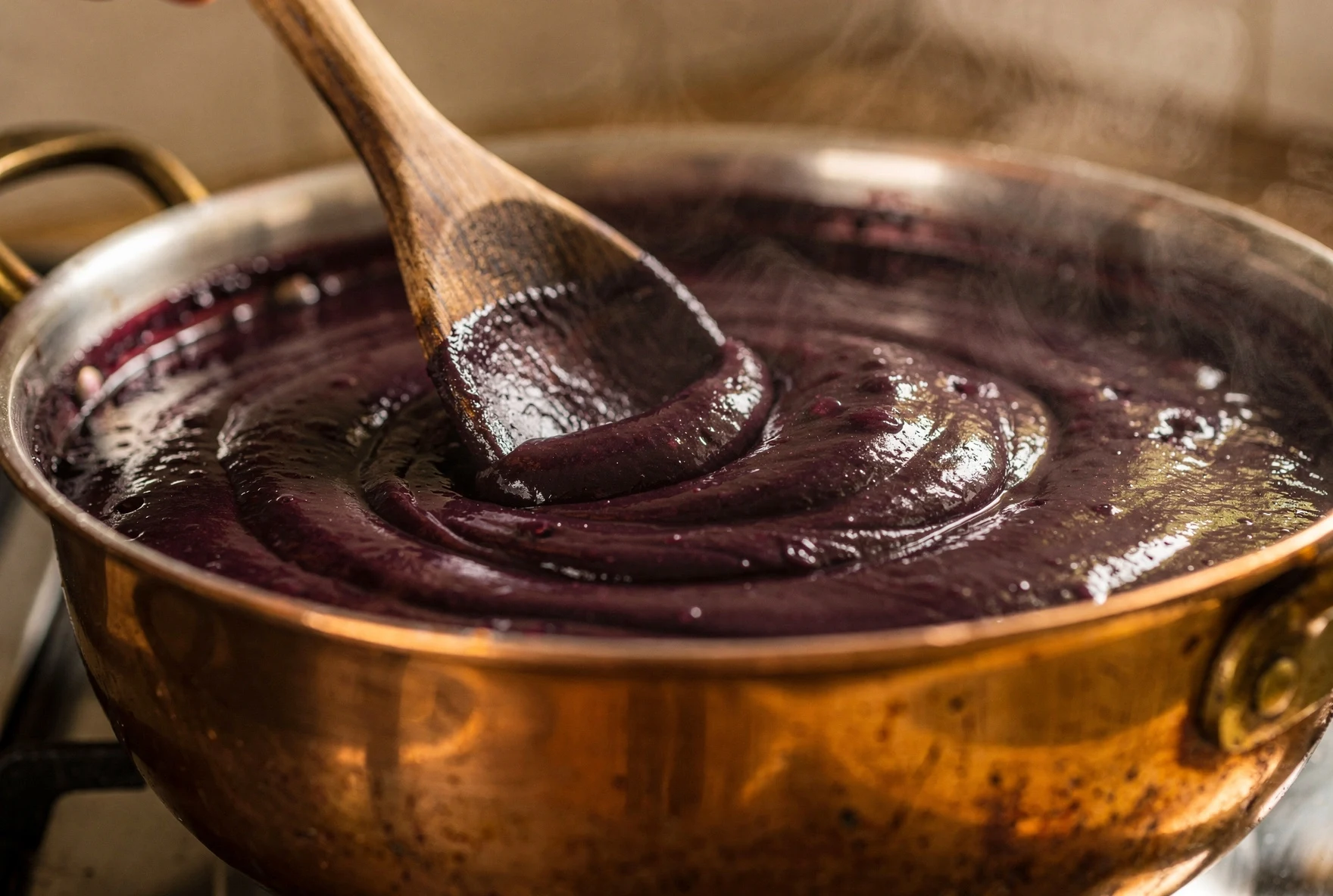 Thick dark purple pelamushi mixture being stirred with a wooden spoon in a heavy pot