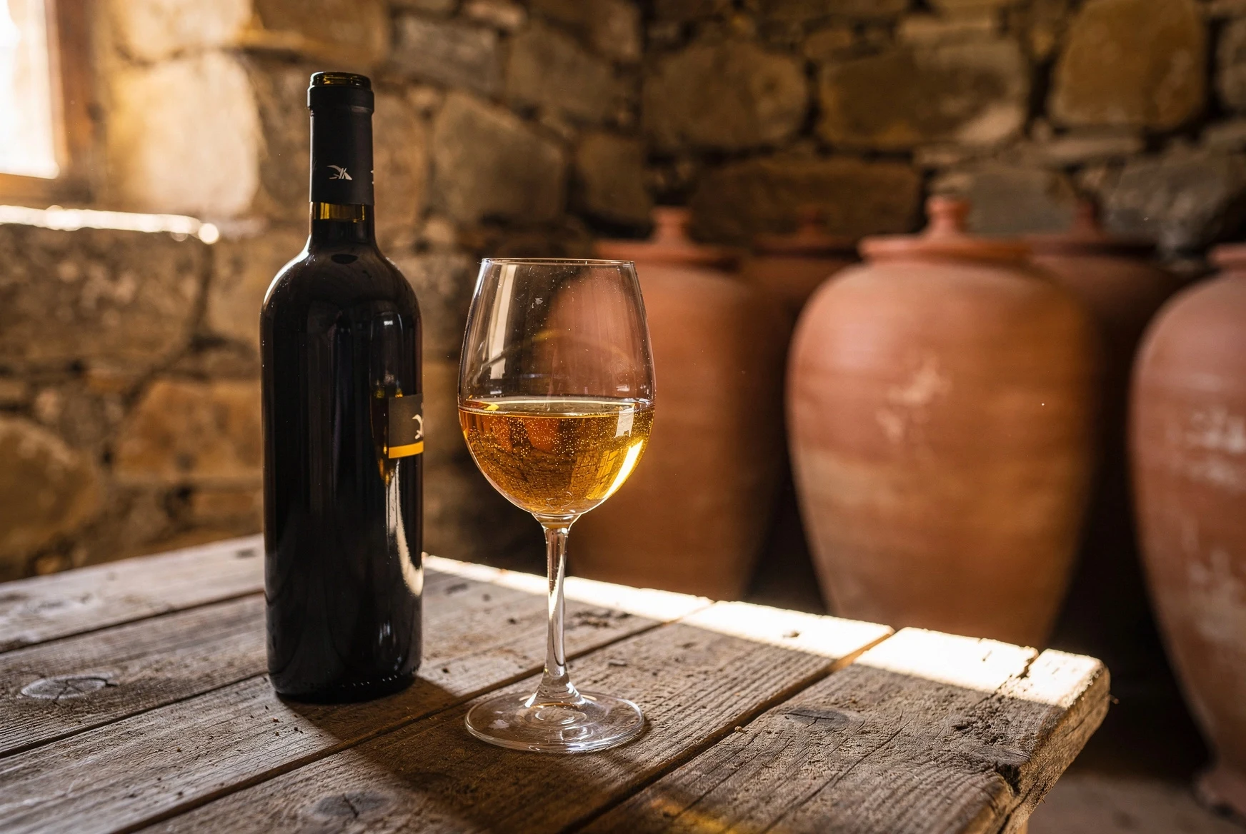 Glass of Georgian Rkatsiteli amber wine beside qvevri cellar vessels