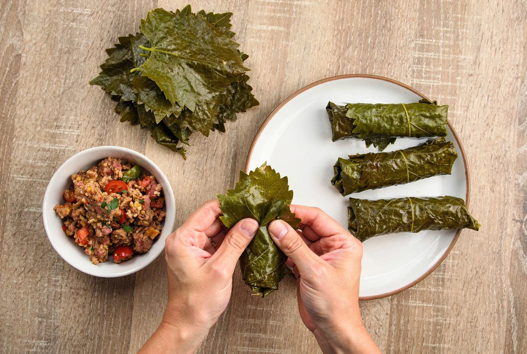 Hands rolling Georgian tolma, showing the technique of folding grape leaves around seasoned meat and rice filling